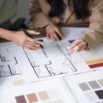 Two female architects discuss interior design building project and use divider compass on blueprint.