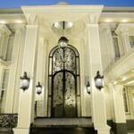 "Elegant exterior of a luxury home with intricate iron gate, grand columns, and modern lighting, showcasing Complete House Construction Solutions in Lahore.