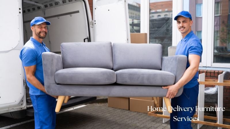 Two professional movers in blue uniforms delivering a grey sofa from a van, showcasing Home Furniture Services in Islamabad, including delivery and setup.