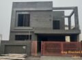 Under-construction grey structure house in Lahore with exposed concrete walls, steel-reinforced windows, and a red gate. Learn about the latest Grey Structure Rate in Lahore.