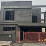 Under-construction grey structure house in Lahore with exposed concrete walls, steel-reinforced windows, and a red gate. Learn about the latest Grey Structure Rate in Lahore.