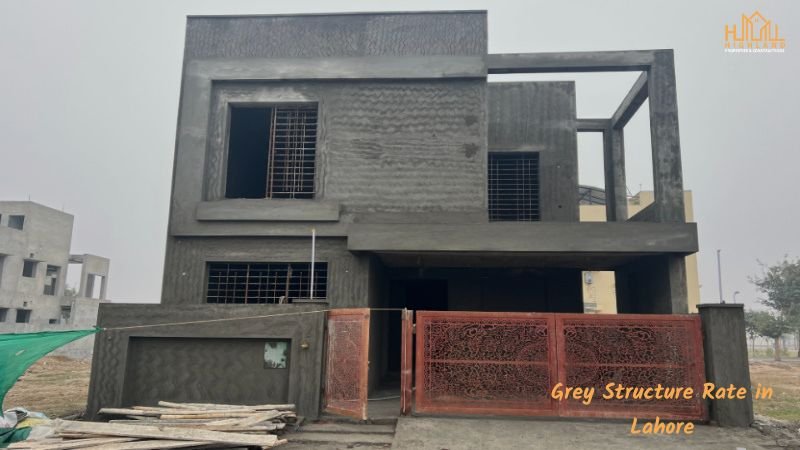 Under-construction grey structure house in Lahore with exposed concrete walls, steel-reinforced windows, and a red gate. Learn about the latest Grey Structure Rate in Lahore.