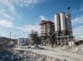 Cement manufacturing plant construction site in Pakistan with large silos, cranes, and industrial structures under a clear sky.