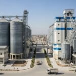 Modern grain rice and flour mill construction in Lahore with steel silos, processing units, and trucks operating on site.