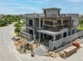 Modern grey structure house construction in Bahria Town Lahore with workers, scaffolding, and construction materials at a residential site