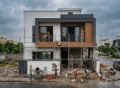 Construction Services in Bahria Town Lahore showing a modern house under construction with workers installing exterior finishes, scaffolding, and contemporary architectural design in progress.
