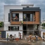 Construction Services in Bahria Town Lahore showing a modern house under construction with workers installing exterior finishes, scaffolding, and contemporary architectural design in progress.