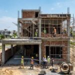 House Construction in DHA Lahore – A modern double-story house under construction with exposed brick walls, concrete framework, scaffolding, and construction workers actively working on-site in a residential DHA Lahore neighborhood.